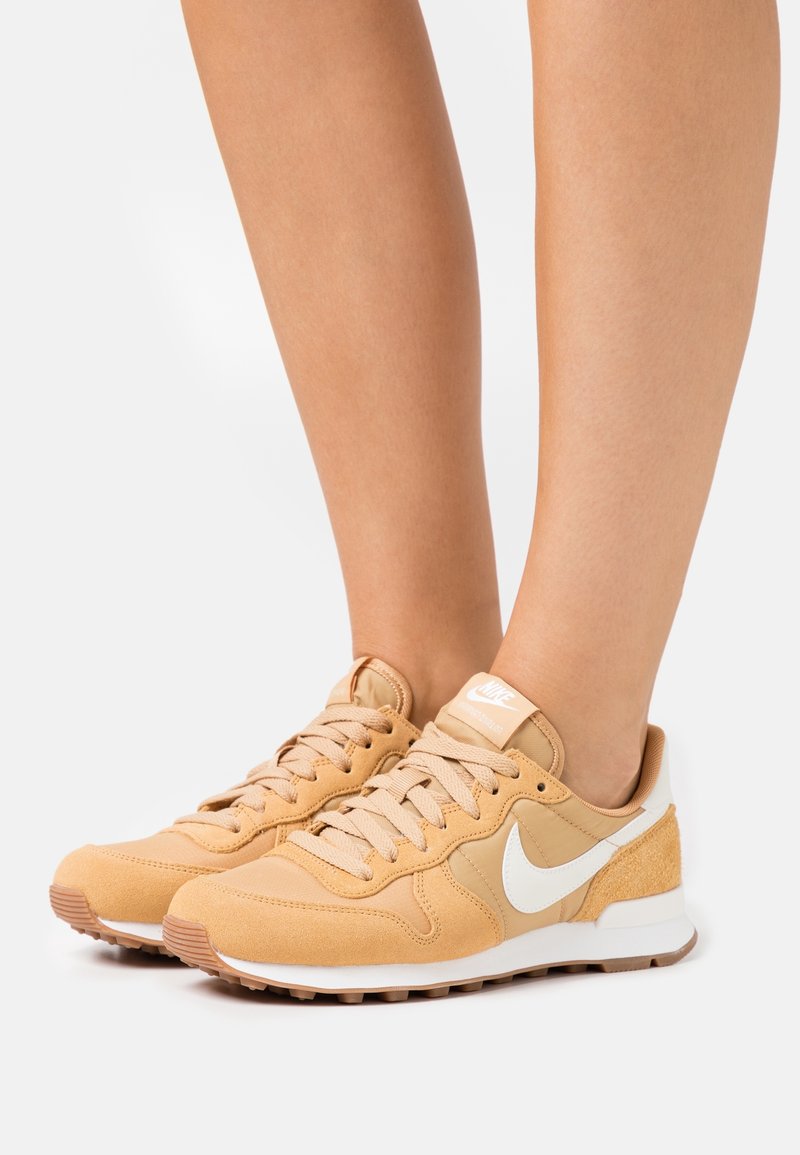 Beige mockasin-sneakers med vita accenter och texturerad detaljer. Har en snörningdesign och en vadderad sula för komfort.