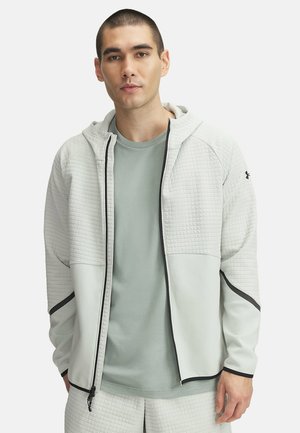 Helle graue Zip-Hoodie aus strukturiertem Stoff mit glattem unteren Abschnitt, kombiniert mit einem hellgrünen T-Shirt. Verfügt über schwarze Akzente.
