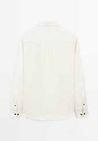 Light beige long-sleeve shirt made of linen, featuring a back pleat, curved hem, and black button accents on the cuffs.