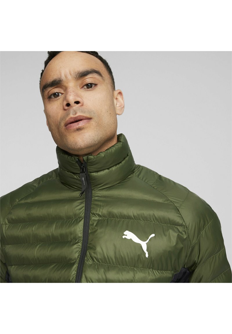 Grøn polstret jakke med høj krave, lynlås foran og sorte detaljer. Har et hvidt Puma-logo på brystet. Letvægts, glat tekstur.