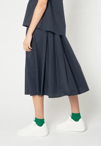 Falda azul oscuro hasta la rodilla con pliegues; combinada con zapatillas blancas y calcetines verdes; diseño minimalista y textura suave.