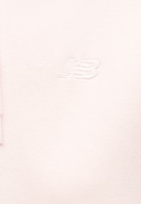 Tissu blanc avec un logo "NB" subtilement en relief, brodé avec un fil blanc assorti.