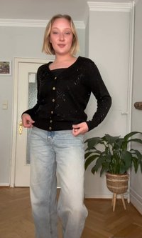 Μαύρο, πλεκτό cardigan με V-neck, διακοσμημένα μοτίβα και χρυσά κουμπιά. Συνδυασμένο με ανοιχτό μπλε, άνετα τζιν. Εσωτερικός χώρος.