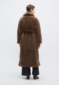 Bruine mantel van namaakbont met een brede kraag, lange mouwen en een ceintuur om te strikken. Heeft een losse pasvorm, valt tot halverwege de kuit en heeft een zachte textuur.