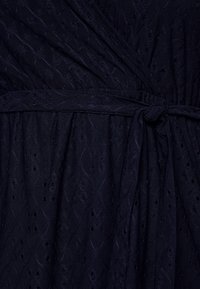 Tummansininen kangas, jossa on silmukkaröyhelö ja texturoitu geometrinen kuvio, sidottuna yksinkertaisella solmulla sopivan kapean vyön kanssa.