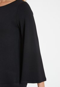 Schwarzes Oberteil aus einem weichen, strukturierten Stoff, mit Dreiviertel-Bellärmeln und rundem Halsausschnitt, entworfen für eine entspannte Passform.