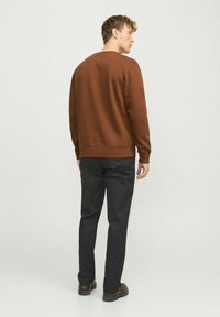 Sudadera marrón de manga larga, cuello redondo y puños de canalé, combinada con pantalones negros y zapatos oscuros, vista desde la parte posterior.