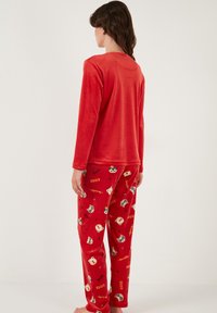 Rote Fleece-Pyjamas mit einem Langarmoberteil und einer Hose, die ein verspieltes Tiermuster und fantasievolle Textdesigns aufweisen. Weiche Textur im gesamten Outfit.