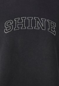 Svart sweatshirt med "SHINE" i rhinestones. Har rund hals og en myk, glatt tekstur. Enkelt design uten ekstra mønstre.