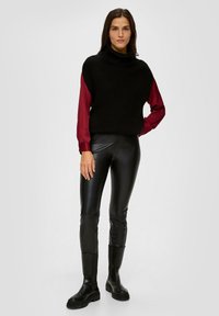 Pull col roulé noir à côtes superposé sur une chemise à manches longues bordeaux, associé à des leggings en similicuir noirs et à des bottes noires chunky.