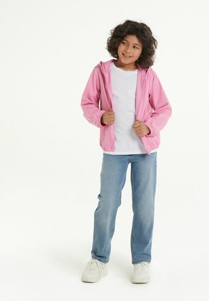 Rosa leichte Jacke mit Kapuze, Reißverschluss vorne und elastischen Bündchen, über einem weißen T-Shirt und blauen Jeans mit weißen Sneakern getragen.