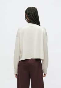 Jasnobeżowy krótki sweter z długimi rękawami, dzianinową fakturą i ściągaczami na mankietach, zestawiony z ciemnym bordowym spodniem. Prosty i funkcjonalny design.