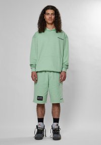 Ljusgrön hoodie med känguruficka, matchande shorts och svarta etikettackcenter. Bärs med högskurna sneakers. Enkel, avslappnad passform.