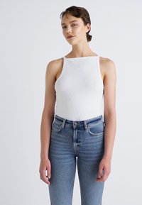 Witte geribde tanktop met brede schouderbanden, gecombineerd met blauw denim jeans met hoge taille, voorzien van een klassiek vijf-pocket ontwerp en een lichte wassing.