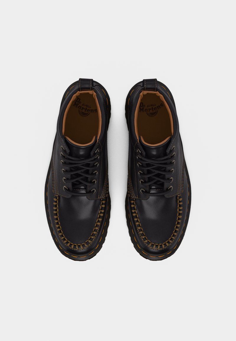 Zwarte leren Dr. Martens veterschoenen met bruine stiksels en trek-lussen, gezien van bovenaf op een witte achtergrond.