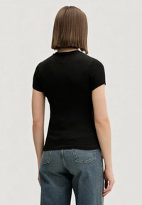 Top nero a maniche corte con costine e design aderente, caratterizzato da una cucitura a V sul retro, abbinato a jeans a vita alta di colore azzurro chiaro.