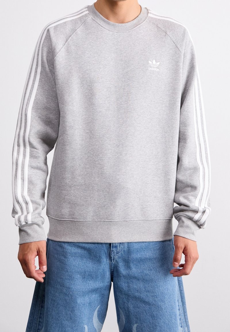 Grå sweatshirts i bomullsmix med vita tre-randiga detaljer längs ärmarna och en liten vit logotyp på bröstet.