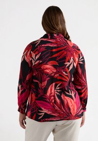 Blusa de manga larga con base negra, que presenta estampados botánicos en rojo y rosa vibrantes. Tejido suave, corte fluido, dobladillo redondeado y puño abotonado.