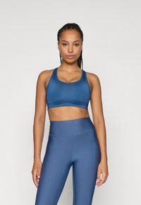 Μπλε αθλητικό σουτιέν και κολάν ψηλής μέσης φτιαγμένα από λείο, ελαστικό ύφασμα. Ο σχεδιασμός είναι εφαρμόστος με στρογγυλή λαιμόκοψη και φαρδιές ράντες.