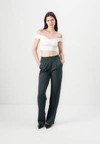 Top court blanc décolleté avec un tissu texturé, associé à un pantalon ample vert foncé doté d'une taille élastique et de poches latérales.