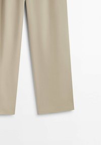 Pantalon beige droit avec une texture de tissu lisse, présenté sur un fond blanc.
