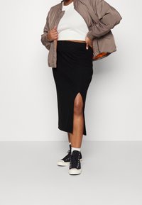 Hnědá bomber bunda s oranžovým podšívkou, bílý crop top, černá sukně ke kolenům s bočním rozparkem a černé vysoké tenisky s bílou podrážkou.