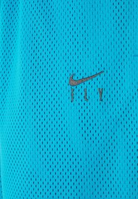 Ljusblått, andningsbart mesh-tyg med svart Nike-swoosh-logga och ordet "FLY" broderat under.