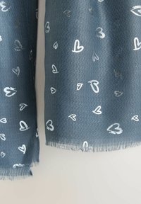 Blåtonet tørklæde lavet af tekstureret stof, der har et herringbone-mønster med spredte hvide hjerteformer og frynsede kanter.