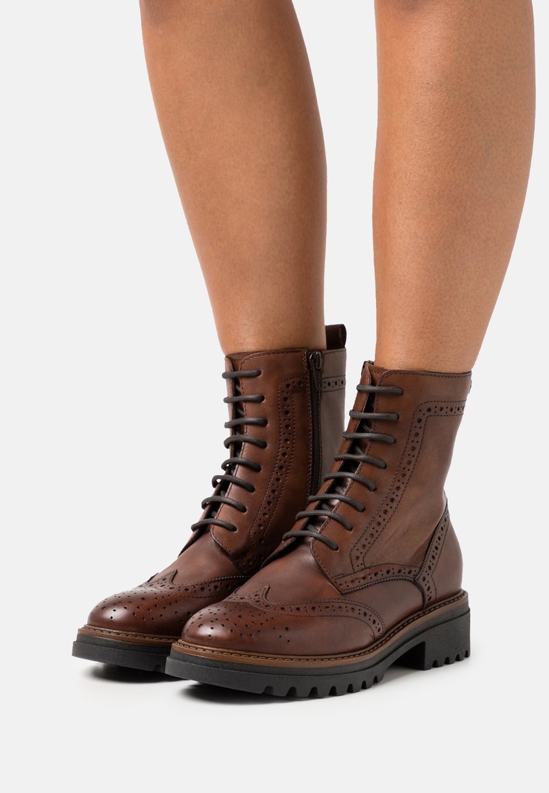 Bottes cheville en cuir marron avec un design brogue, comprenant des lacets, une fermeture éclair latérale et une semelle robuste pour une bonne adhérence.