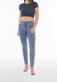 Smala jeans i ljusblå denim med hög midja, två framfickor och knappstängning. Matchas med en kort marinblå figurpassad topp och sandaler.