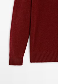Burgundy tröja med ärm gjord av mjukt, texturerat tyg med ribbade ärmslut och en något lös design. Inga synliga mönster eller hårdvara.