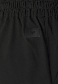 Black shorts made of lightweight fabric with an elastic waistband, featuring a small textured logo patch on the back.