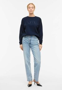 Sweat-shirt marine avec "LOVE" brodé sur le devant, associé à un jean droit bleu clair et des mules noires à talons. Texture lisse, coupe décontractée.