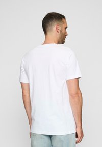 Hvid bomulds t-shirt vist fra bagsiden, med rund hals og korte ærmer, lige kant og enkel design.