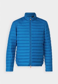 Blauwe pufferjack met een hoge kraag, horizontaal gestikt patroon, volledige rits en een oranje ritsaccent. Zacht, lichtgewicht materiaal.