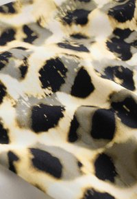 Tkanina z leopardjim vzorom, ki ima velike črne lise na bež ozadju, z gladko teksturo in mehkoben draperijem.