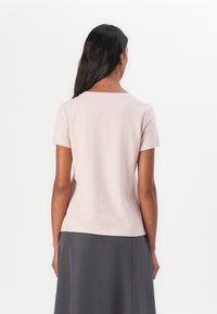 Kurzärmliges, pastellpinkes T-Shirt aus weichem Stoff. Es hat einen klassischen Rundhalsausschnitt und einen lockeren Schnitt. Rückansicht gezeigt.