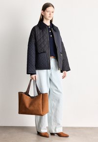 Σκούρο μπλε μπουφάν καπιτονέ με γιακά, συνδυασμένο με μπλε ναυτικό πουλόβερ, ανοιχτό μπλε τζιν παντελόνι με φαρδιά μπατζάκια και καφέ τσάντα ώμου από σουέντ. Καφέ παπούτσια με τακούνι.