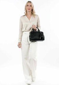 Svart texturerad handväska med dubbla handtag, blixtlåsstängning och en liten bifogad påse, tillsammans med en beige blus och vita byxor.