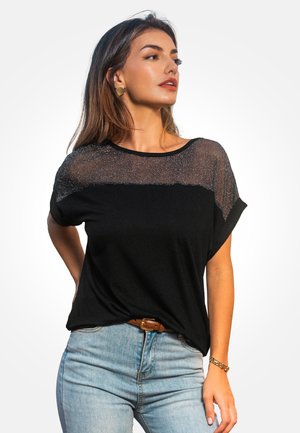 T-shirt noir avec un panneau transparent et scintillant en haut, manches courtes et coupe décontractée, associé à un jean taille haute bleu clair.