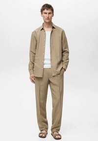 Beige stribet skjorte og matchende bukser lavet af et let stof, stylet med en enkel hvid tanktop og brune sandaler.