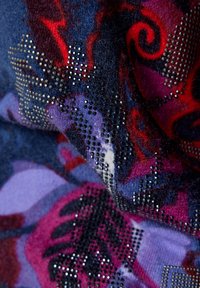 Textured wool blend fabric featuring a floral pattern in red and purple, embellished with metallic studs. Rich colors with intricate design.