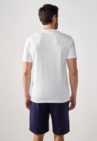 Hvid t-shirt med korte ærmer og rund udskæring, parret med navy shorts. Stoffet ser glat ud med en blød tekstur.
