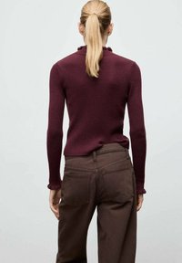 Haut en maille côtelée merlot avec un col volant, associé à un pantalon taille haute marron. Le tissu est doux avec une texture lisse.