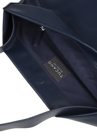 Navy blauwe leren tas interieur met een gladde textuur, voorzien van een ritsvak en een merketiket, aangevuld met een zachte stoffen voering.