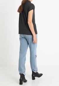 Tmavě šedé tričko s krátkým rukávem v kombinaci s světle modrými roztrhanými džíny a černými koženými kotníkovými botami na podpatku; hladký materiál a volný střih.