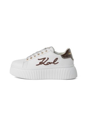 Fehér sneaker vastag, bordázott talppal, amelyen egy barna, varrott "Karl" logó található, ezüst szemes fűzőkkel és barna díszítéssel a sarokon.