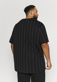 Chemise noire à manches courtes avec des rayures verticales bleu foncé. Coupe ample, col rond, tissu doux et ourlet plat en bas.