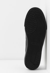 Semelle de sneaker noire avec un motif texturé, présentant un design en vagues. Le matériau semble être du caoutchouc avec un marquage en relief sur le côté.