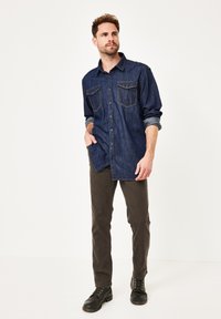 Dunkelblaue Denim-Bluse mit zwei Brusttaschen, Knopfverschluss, hochgerollten Ärmeln. Kombiniert mit olivgrünen Hosen und schwarzen Schnürstiefeln.